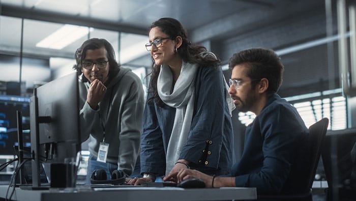 Three developers work together around a computer, building an IoT solution and accessing technical documentation through Bell's Developer Hub.