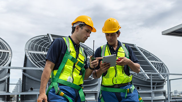 Two field workers in safety gear using a tablet with Bell's mobile workforce management software to coordinate tasks.