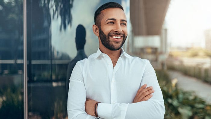 A smiling business professional stands confidently in front of a modern glass building, representing the discovery of IoT executive insights and business transformation trends.